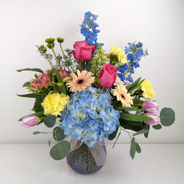 Mixed bouquet with blue hydrangea, pink roses, and yellow carnations in a glass vase
