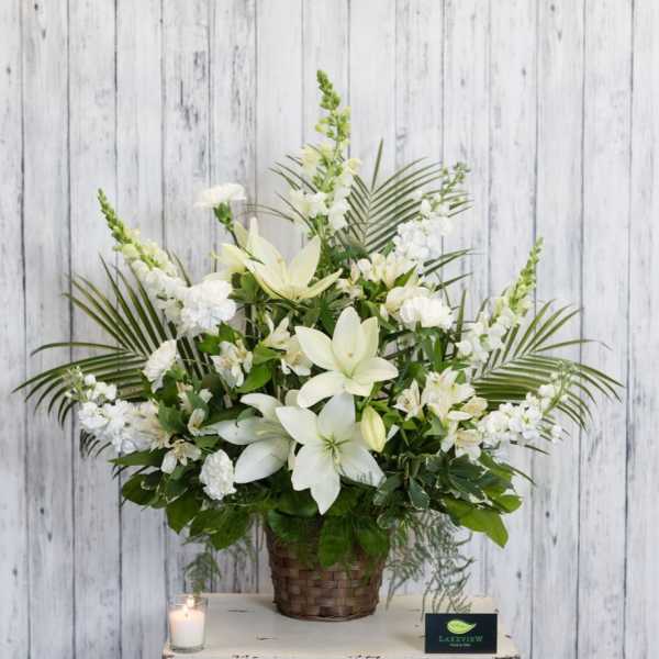 White floral arrangement in a woven basket with a candle beside it