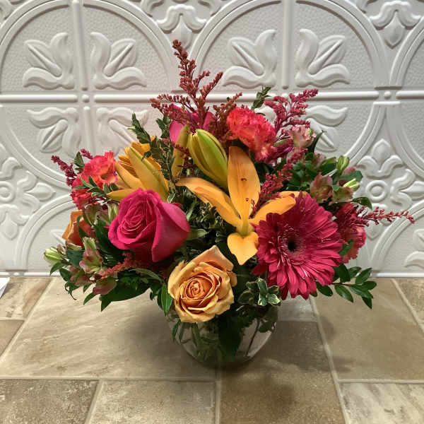 Mixed bouquet of pink, orange, and yellow flowers in a glass vase