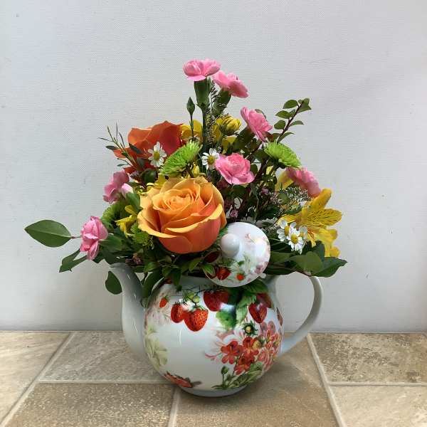 Mixed bouquet of roses, daisies, and carnations in a strawberry-patterned teapot