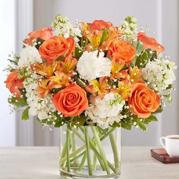 Orange roses and white flowers arranged in a clear glass vase