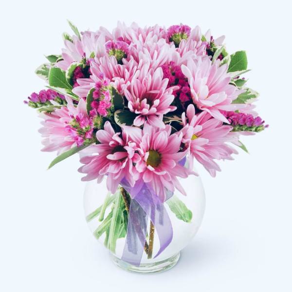 Pink daisy bouquet in a clear glass vase with a purple ribbon