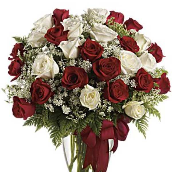 Red and white roses in a clear glass vase with a red ribbon