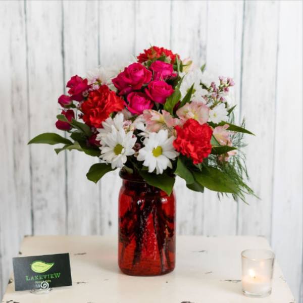 Mixed bouquet in a red glass vase with a lit candle nearby