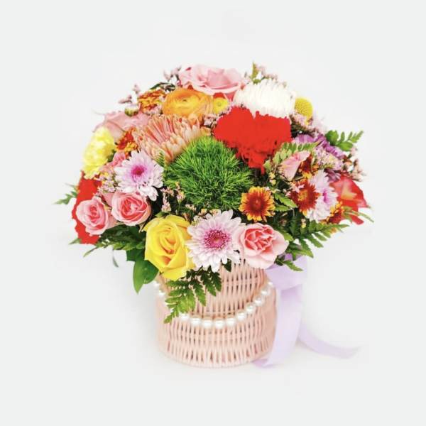 Colorful mixed flower bouquet in a wicker basket with a ribbon