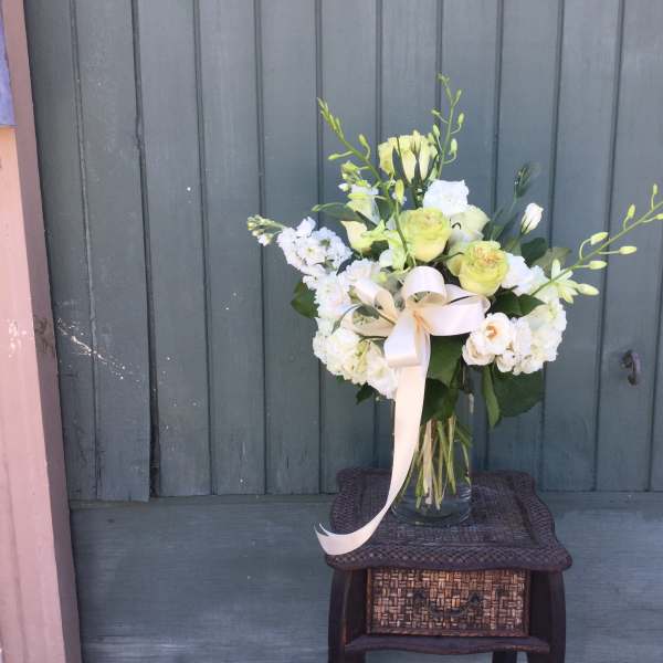 White and pale green floral arrangement in a glass vase with a ribbon
