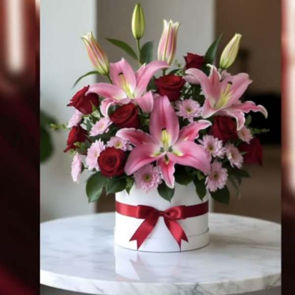 Pink lilies and red roses in a white hatbox with a red ribbon