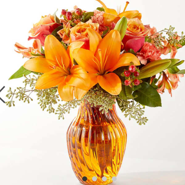 Orange lilies and roses arranged in an amber glass vase