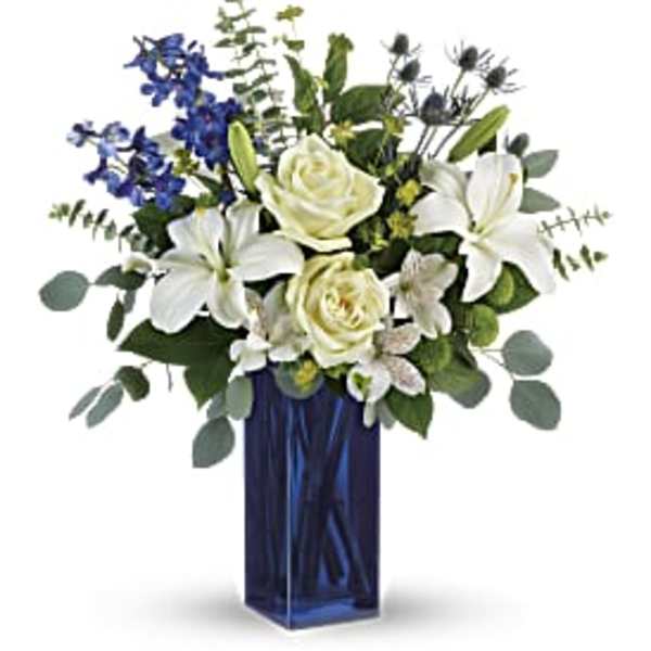 White lilies and roses in a tall blue vase with blue flowers