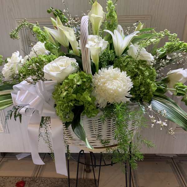 White lilies and chrysanthemums in a white basket with a ribbon
