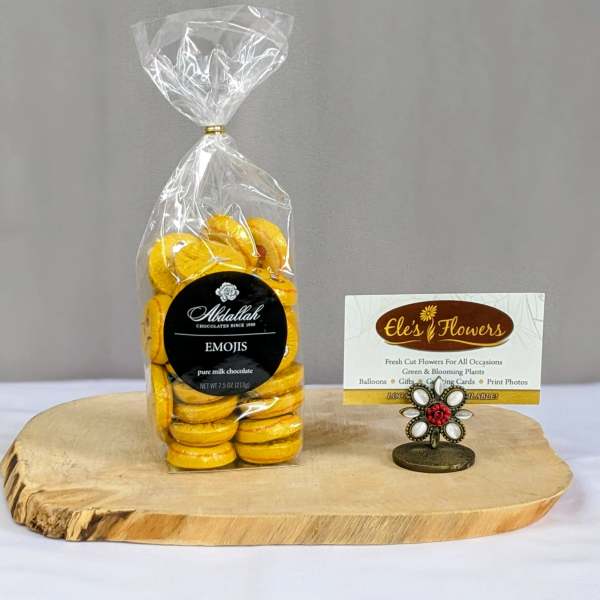 Bag of yellow emoji chocolates on a wood slab with a decorative business card holder