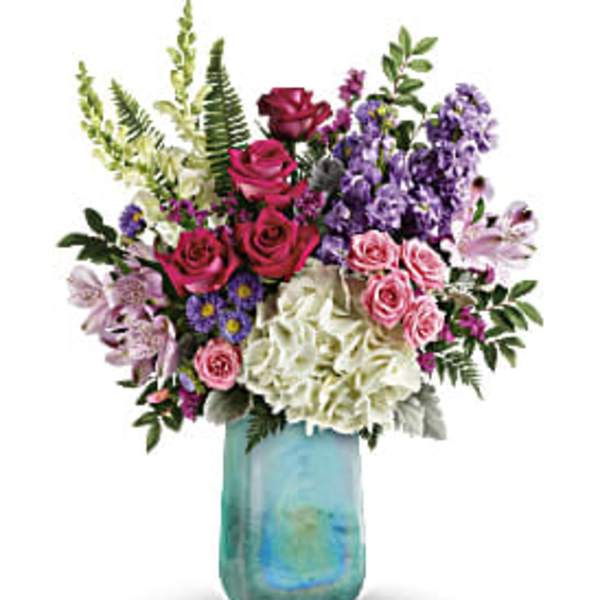Mixed bouquet of roses, hydrangeas, and purple flowers in a blue glass vase