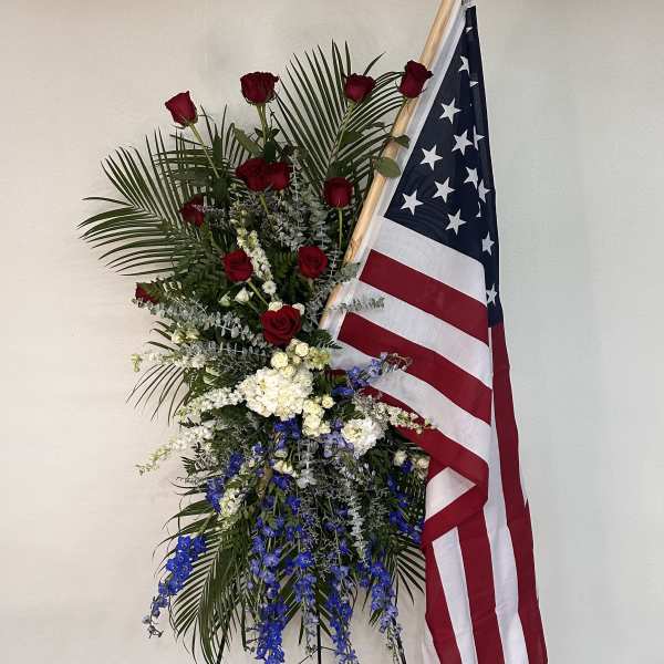 Standing floral spray with red, white, and blue flowers beside an American flag