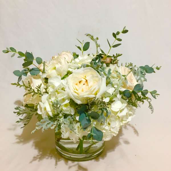 Low white and cream rose and hydrangea arrangement in a clear glass cylinder vase