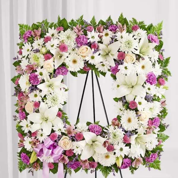 Floral wreath on a black stand with white and pink flowers and a lavender ribbon