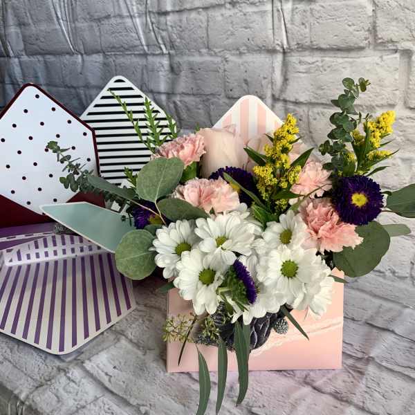 Mixed bouquet of white daisies, pink carnations, and purple flowers in a pastel gift box