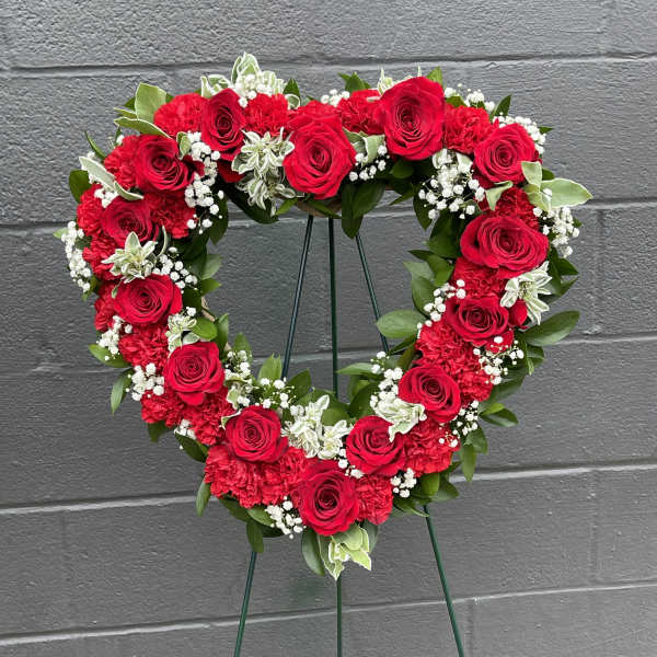 Heart-shaped floral wreath with red roses and white filler flowers on a stand