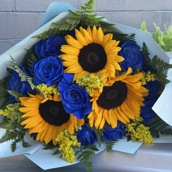 Bouquet of blue roses and yellow sunflowers wrapped in pale blue paper