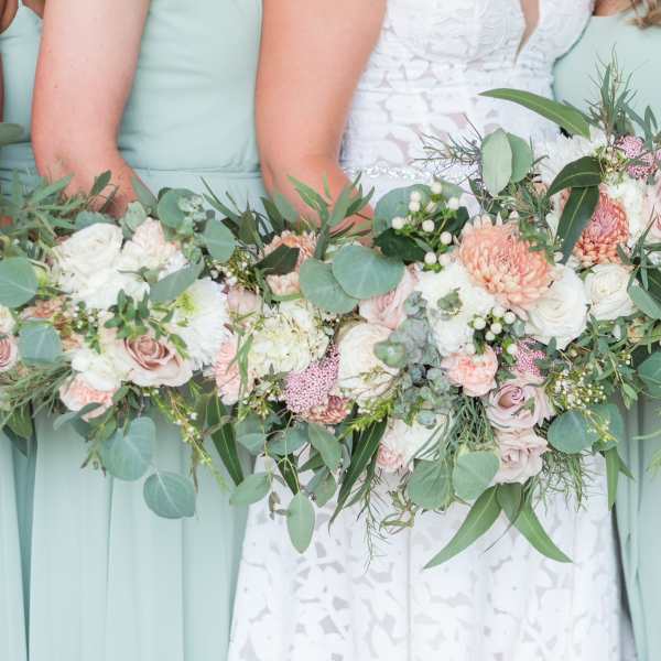 Bridesmaids holding pastel bouquets with roses and greenery