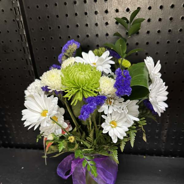 White daisies and purple flowers in a small vase with a purple ribbon