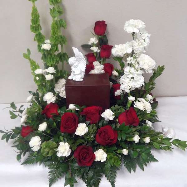 Red roses and white flowers arranged around a small urn with a figurine