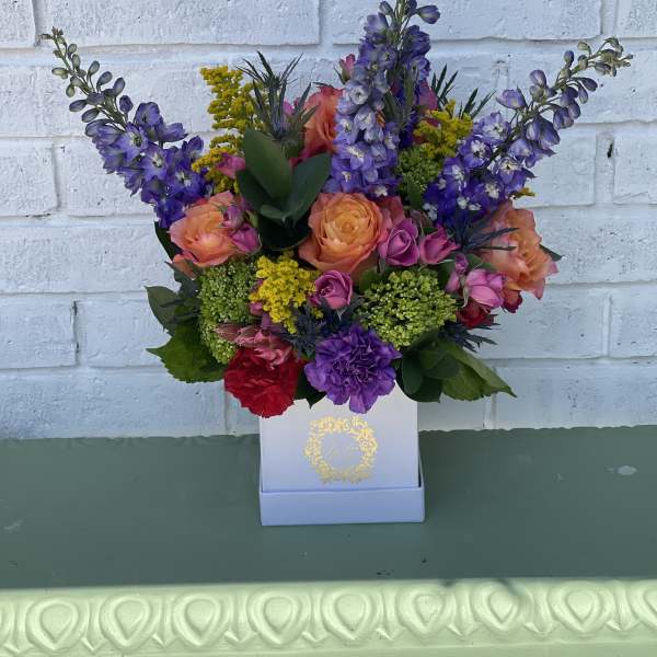 Colorful bouquet of purple, peach, and pink flowers in a white box