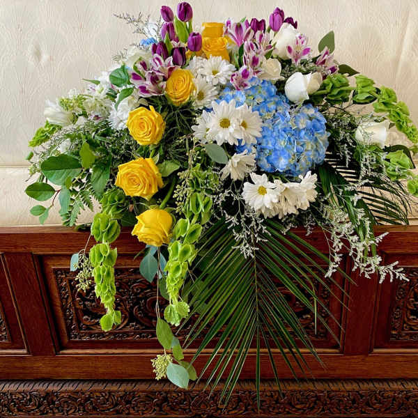 Large floral spray with yellow roses, blue hydrangeas, and white daisies