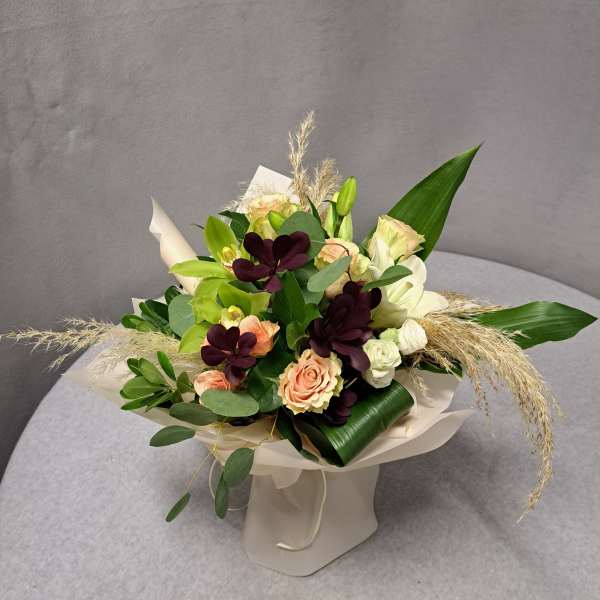 Bouquet of peach and white roses with dark purple flowers in cream wrap