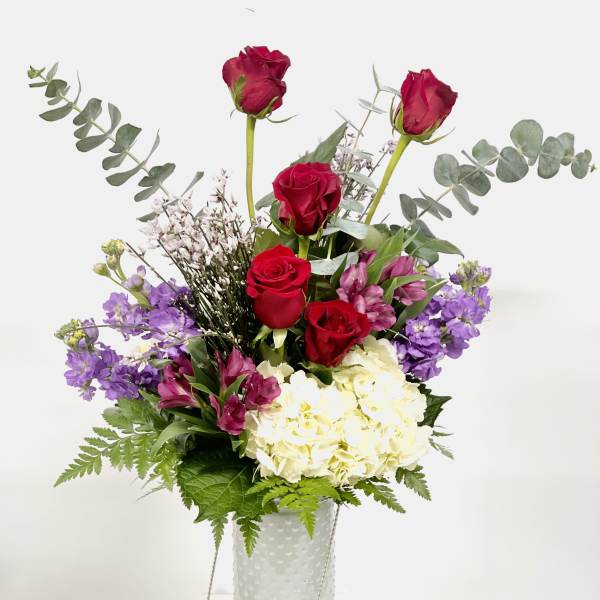 Red roses and purple flowers in a white vase