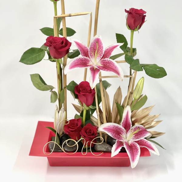 Red roses and pink lilies in a red rectangular vase with bamboo accents