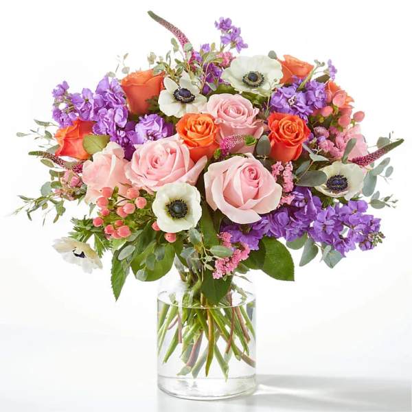Bouquet of pink and orange roses with purple flowers in a clear glass vase