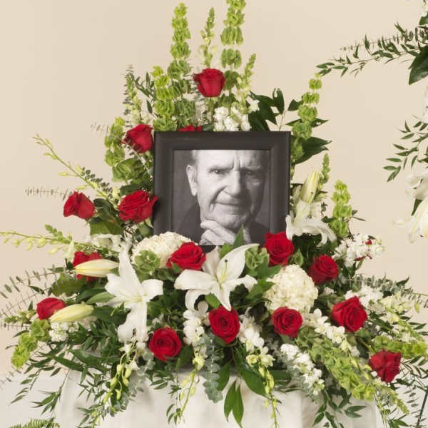 Sympathy floral display with red roses, white lilies, and a framed portrait