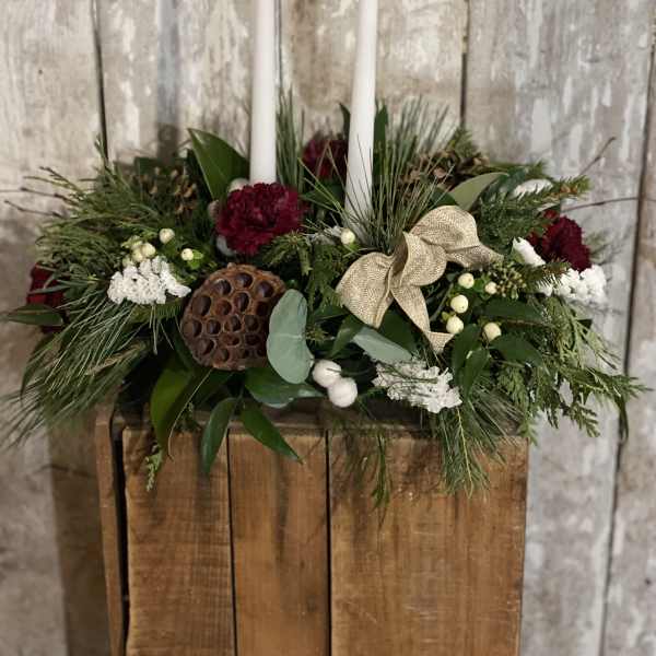 Holiday centerpiece with white candles, red flowers, and greenery in a wooden box