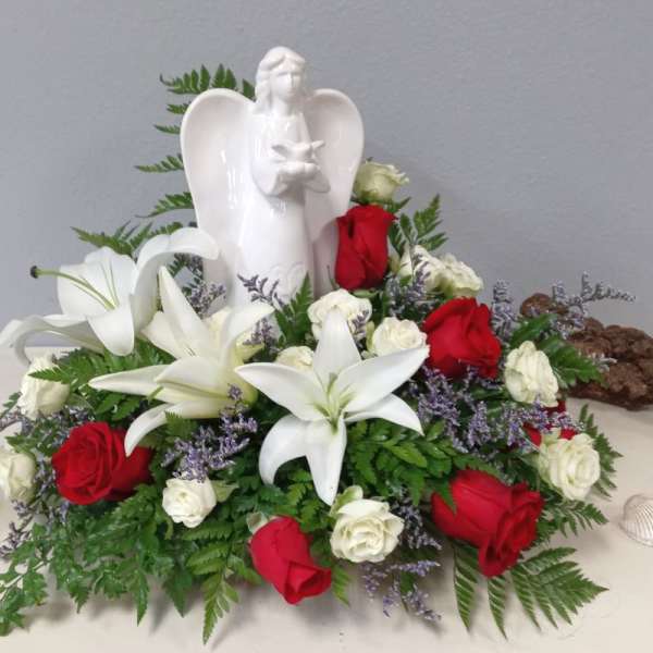 White lilies and red roses arranged around a white angel figurine