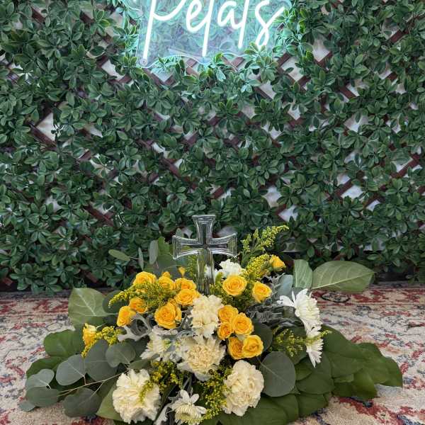 Yellow and white floral arrangement with a clear cross in front of a green wall