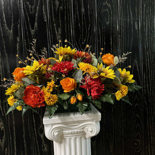 Bright orange and yellow floral arrangement on a white pedestal