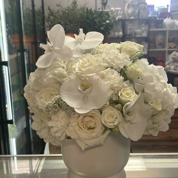White floral arrangement in a round vase with orchids and roses