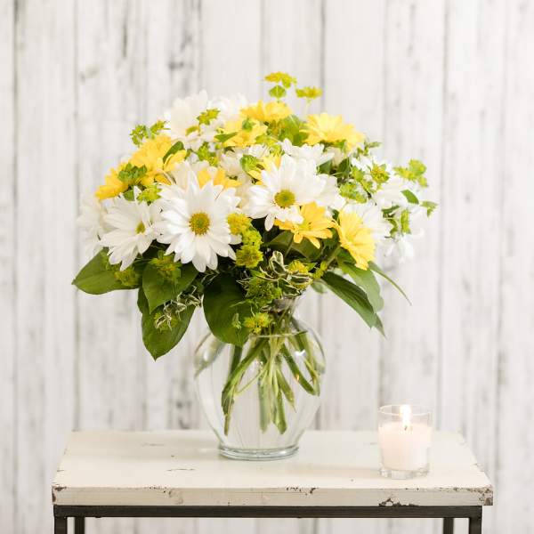 White and yellow daisy bouquet in a glass vase beside a candle