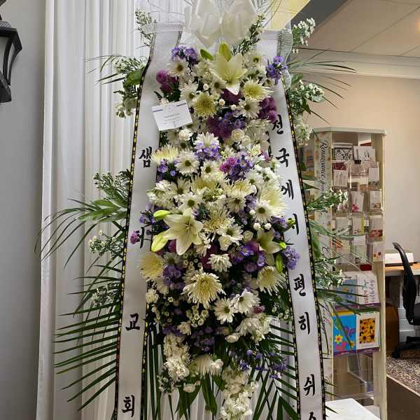 Tall standing floral wreath with white and purple flowers and ribbon streamers