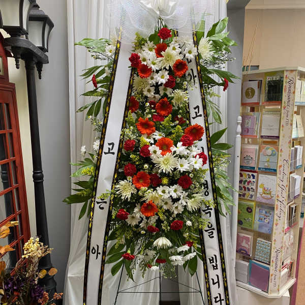 Tall standing floral spray with white ribbons and red, white, and orange flowers