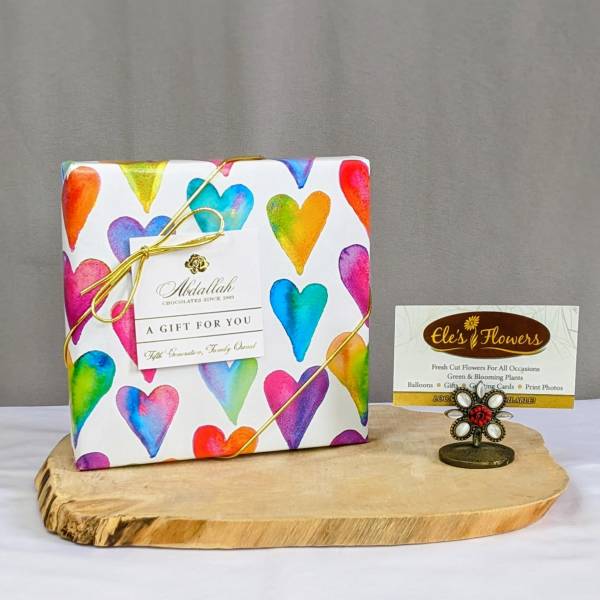 Heart-patterned chocolate gift box on a wooden board with a small flower-shaped card holder.