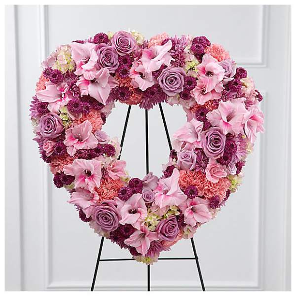 Heart-shaped floral wreath in pink and lavender tones on a black stand