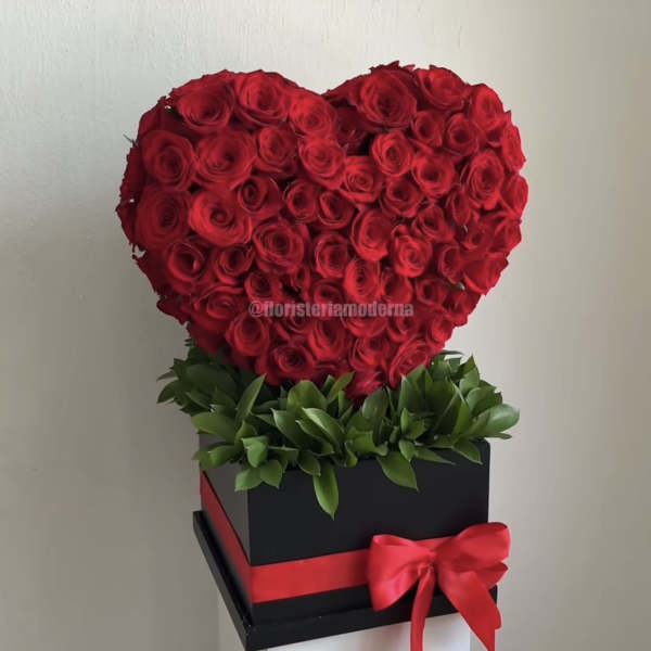 Heart-shaped arrangement of red roses in a black box with a red ribbon