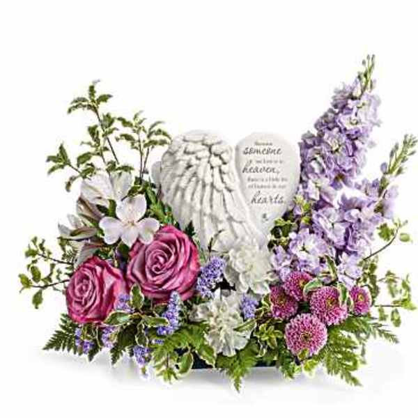 Low arrangement of pink and purple flowers surrounding a white angel-wing heart plaque.