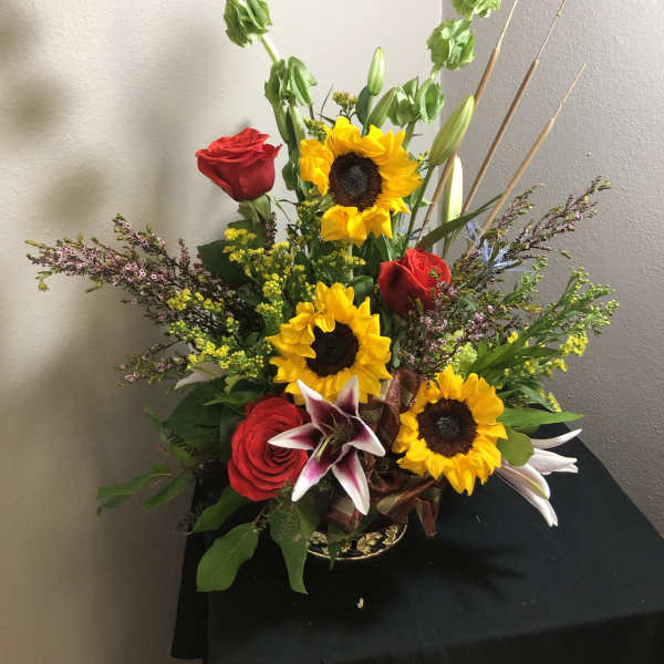 Tall mixed bouquet with sunflowers, red roses, and lilies in a vase