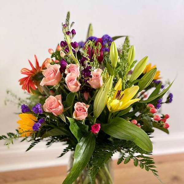 Mixed bouquet of pink roses, yellow lilies, and purple flowers in a glass vase