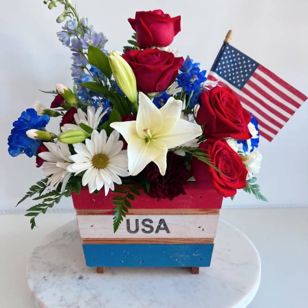 Red roses and white lilies in a patriotic wooden container with a small U.S. flag.