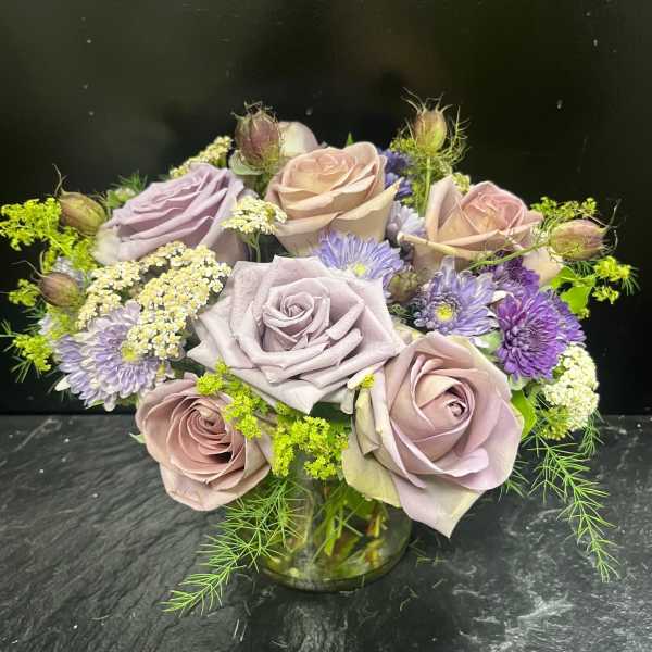 Lavender and blush roses with purple daisies in a glass vase