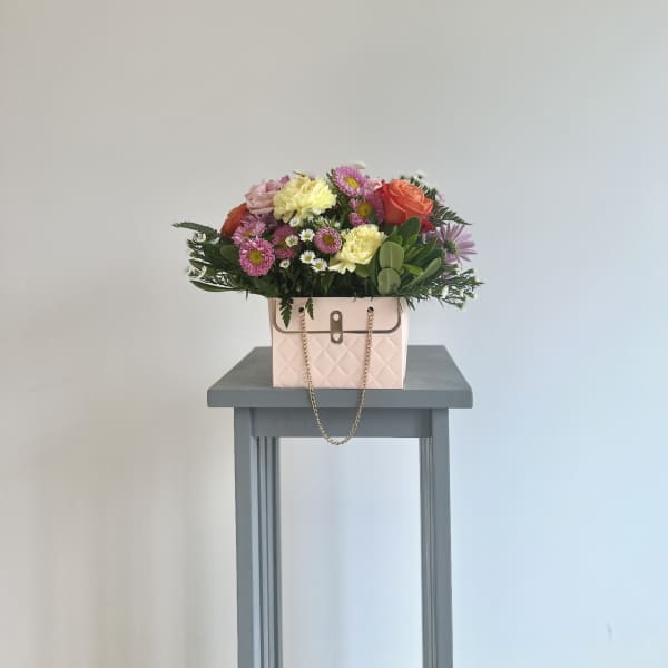 Mixed bouquet in a pink handbag-style container on a small table