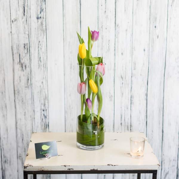 Tall glass vase with colorful tulips and green leaves